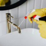 Ruke u rukavicama za čišćenje koje prskaju sredstvo po slavini
